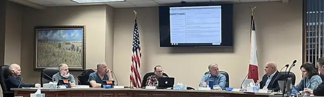 County board meeting with documents displayed on the room screen